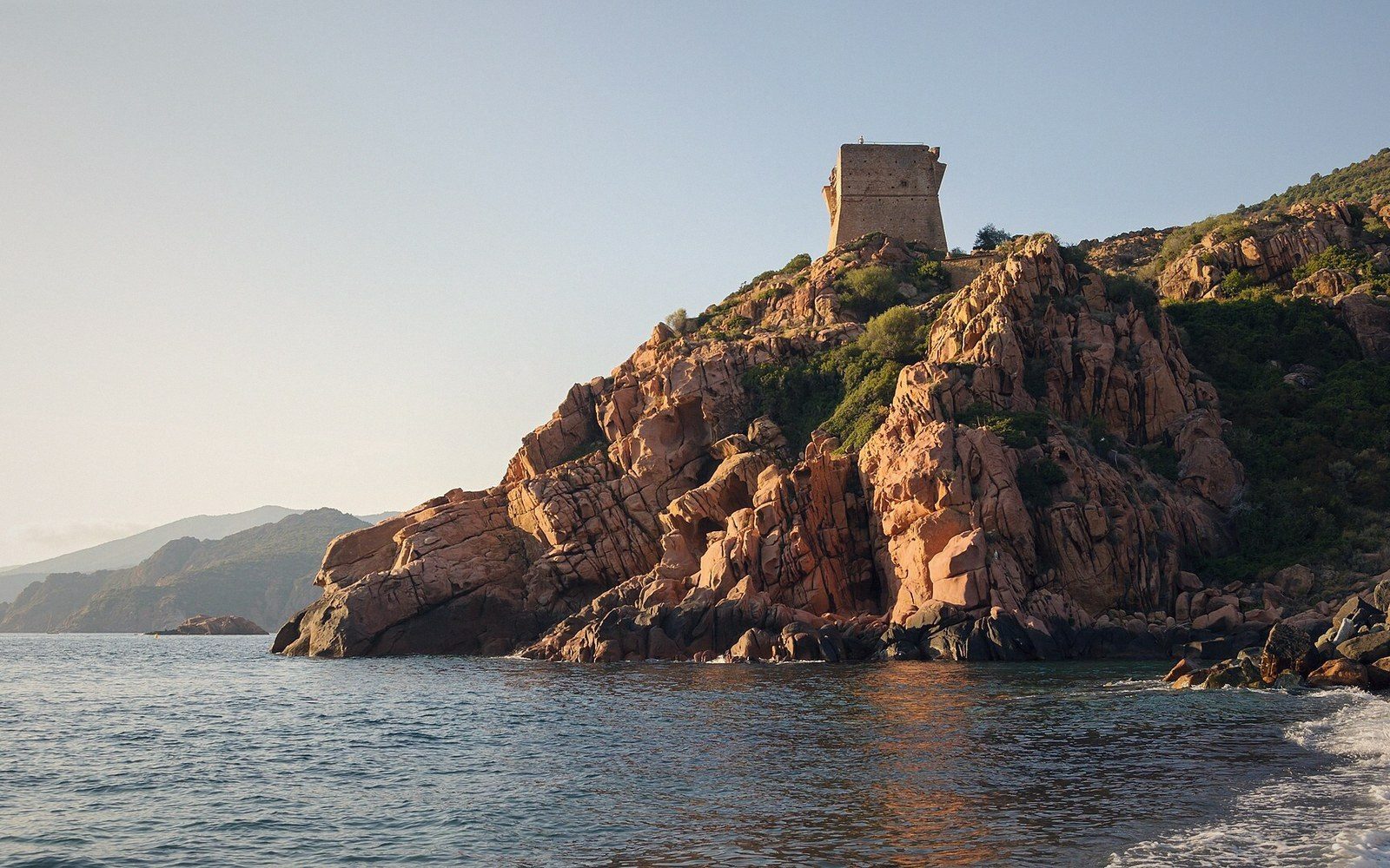 A stone watchtower crowns red rocky cliffs above the sea