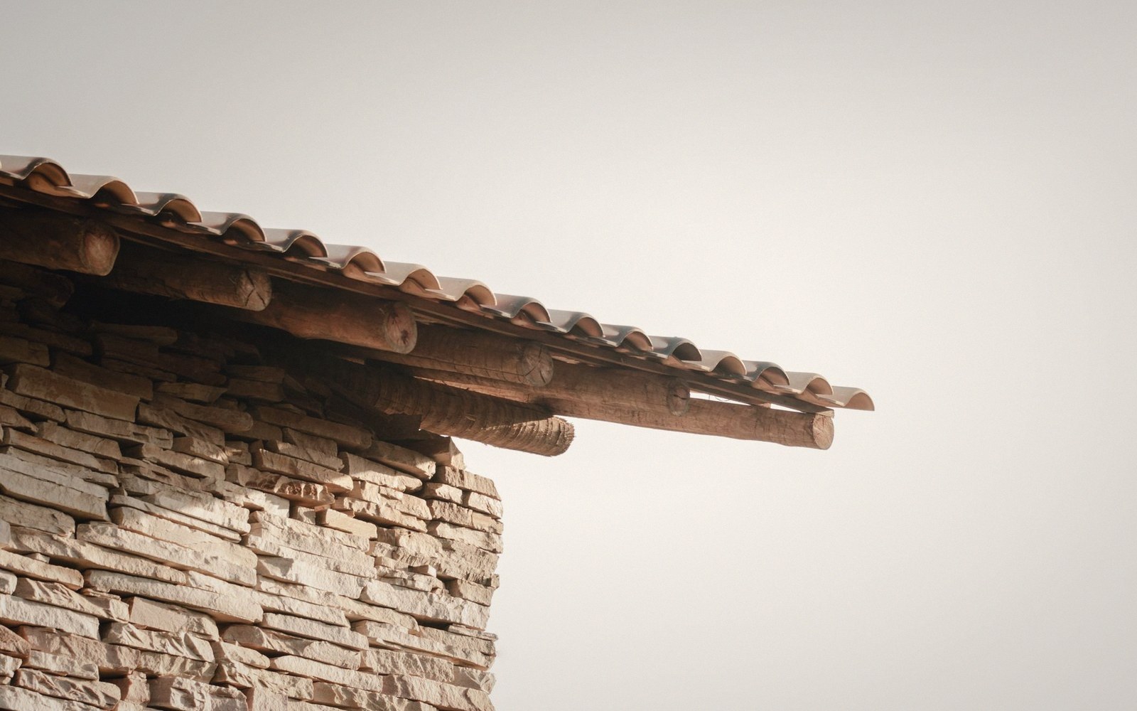 Wooden roof beams project beyond a dry stone wall under a curved tile roof
