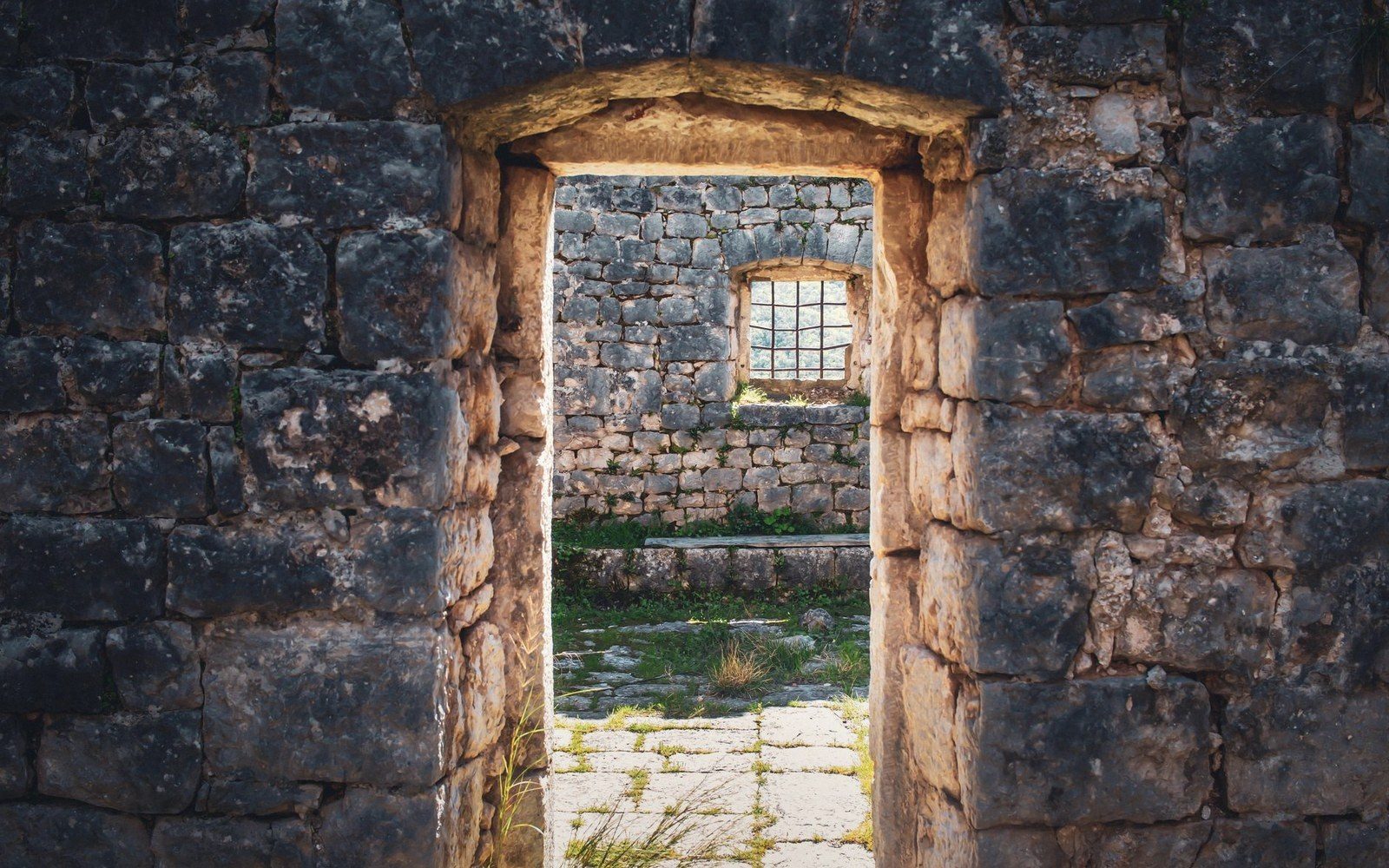 Stone archway frames a roofless ruined room with a small barred window
